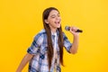 happy young girl singer perform karaoke isolated on yellow background. With microphone in hand teenage girl singer