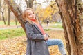 Happy young girl smiling and sitting on tree in beautiful autumn park on nature walks outdoors. Little child playing in Royalty Free Stock Photo