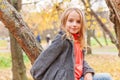 Happy young girl smiling and sitting on tree in beautiful autumn park on nature walks outdoors. Little child playing in autumn Royalty Free Stock Photo