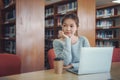 Happy young girl student studying at the college library, sitting at the desk, using laptop computer Royalty Free Stock Photo