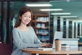 Happy young girl student studying at the college library, sitting at the desk, using laptop computer Royalty Free Stock Photo