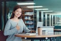 Happy young girl student studying at the college library, sitting at the desk, using laptop computer Royalty Free Stock Photo