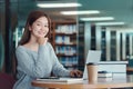 Happy young girl student studying at the college library, sitting at the desk, using laptop computer Royalty Free Stock Photo