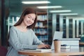 Happy young girl student studying at the college library, sitting at the desk, using laptop computer Royalty Free Stock Photo