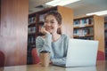 Happy young girl student studying at the college library, sitting at the desk, using laptop computer Royalty Free Stock Photo