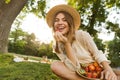 Happy young girl in summer hat having a picnic at the park, sitting on a grass Royalty Free Stock Photo