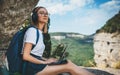 Happy young girl tourist with backpack enjoying summer holidays listen music in headphones and laptop in nature, woman copywriter Royalty Free Stock Photo