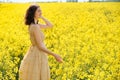 Happy young girl walking in canola field on summer day. Beautiful woman in beige dress enjoying nature Royalty Free Stock Photo