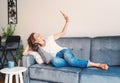 Happy young girl woman in jeans and white t-shirt makes selfie on the couch at home, internet and technology, video chat Royalty Free Stock Photo