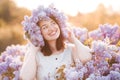 Happy young girl 28-30 year old wear floral wreath with lilac flowers posing in blooming meadow over nature background close up Royalty Free Stock Photo