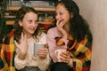 Happy young girls friends talking and laughing sitting wrapped in a blanket in home. Royalty Free Stock Photo