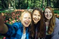 Happy young girls have fun laughing and taking selfies on a smartphone in the park on the background of green foliage and flowers
