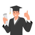 Happy young graduate man in graduation gown and hat holding diploma and certificate showing thumb up