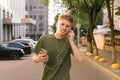 Happy young guy in a green T-shirt strolling around the city with a smartphone in his hands, listening to music in the headphones Royalty Free Stock Photo