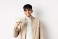 Happy young guy holding dollar bills and smiling, making money and looking cheerful at camera, standing on white Royalty Free Stock Photo