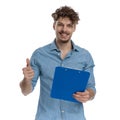 Happy young guy making thumbs up sign and holding clipboard Royalty Free Stock Photo