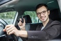 Happy young guy is sitting at his car while looking at the camera. He is holding the keys in his right hand. His left hand is on Royalty Free Stock Photo