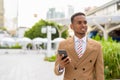 Happy young handsome African businessman thinking while using phone in the city Royalty Free Stock Photo