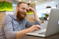 Happy young handsome caucasian american man in shirt laughing watching at laptop sitting indoors restaurant during online chat Royalty Free Stock Photo