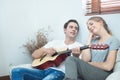 Happy young handsome caucasian man play guitar and sing song for his girlfriend sit in sofa in living room at apartment.Hipster Royalty Free Stock Photo