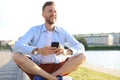 Happy young handsome man sitting on the bench outdoors and using smartphone Royalty Free Stock Photo