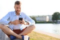 Happy young handsome man sitting on the bench outdoors and using smartphone Royalty Free Stock Photo