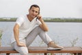 Happy young handsome man sitting on the bench outdoors and using smartphone Royalty Free Stock Photo