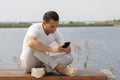 Happy young handsome man sitting on the bench outdoors and using smartphone Royalty Free Stock Photo