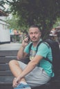 Happy young handsome man sitting on the bench outdoors and using smartphone. Tropical island of Bali, Indonesia. Royalty Free Stock Photo