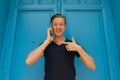 Happy young handsome man talking on mobile phone and pointing finger in front of blue door Royalty Free Stock Photo