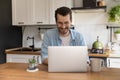 Happy young handsome man using computer in kitchen. Royalty Free Stock Photo