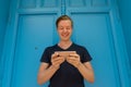 Happy young handsome man using mobile phone in front of blue door Royalty Free Stock Photo