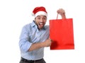 Happy young handsome man wearing santa hat holding red shopping bag Royalty Free Stock Photo