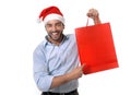 Happy young handsome man wearing santa hat holding red shopping bag Royalty Free Stock Photo