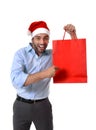 Happy young handsome man wearing santa hat holding red shopping bag Royalty Free Stock Photo