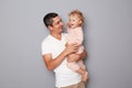 Happy young handsome man in white T-shirt holding little toddler girl standing isolated over gray background having funny time Royalty Free Stock Photo