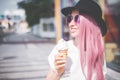 Happy young hipster woman with long pink hair, hat and sunglasses eating ice cream outdoors