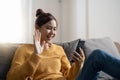 Happy young hispanic asian teen girl sit on sofa at home holding phone looking at screen waving hand video calling Royalty Free Stock Photo