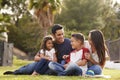 Happy young Hispanic family sitting together on the grass in the park, looking at each other