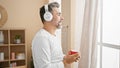 Happy young hispanic man, grey-haired and handsome, casually drinking coffee and enjoying music at home in the morning, listening Royalty Free Stock Photo