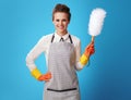 Happy young housemaid with dust cleaning brush on blue