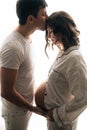 Happy young husband kissing his pregnant wife and holding belly bump. Stylish pregnant family, mom and dad in white pajamas, Royalty Free Stock Photo