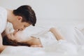 Happy young husband kissing his smiling pregnant wife lying on white bed and hugging baby belly bump. Stylish pregnant couple in Royalty Free Stock Photo