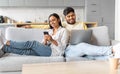 Happy Young Indian Couple Relaxing With Modern Gadgets On Couch At Home Royalty Free Stock Photo