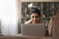 Happy young indian female enjoy using pc lying on sofa