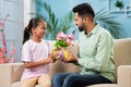 Happy young Indian girl kid giving flowers with gift to father while sitting on sofa at home - concept of father& x27;s Royalty Free Stock Photo