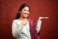 Happy young indian Girl looking camera by showing empty hand and pointing finger - concept of product sales, promotions, offers