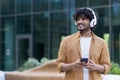 Happy young Indian man listening to music, podcast on his phone. Standing outside wearing headphones and looking away Royalty Free Stock Photo