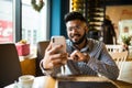 Happy young indian man sitting at cafe making video call from his mobile phone. Asian male at coffee shop having a videochat on Royalty Free Stock Photo