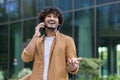 A happy young Indian man is standing on a city street and talking emotionally on a mobile phone Royalty Free Stock Photo